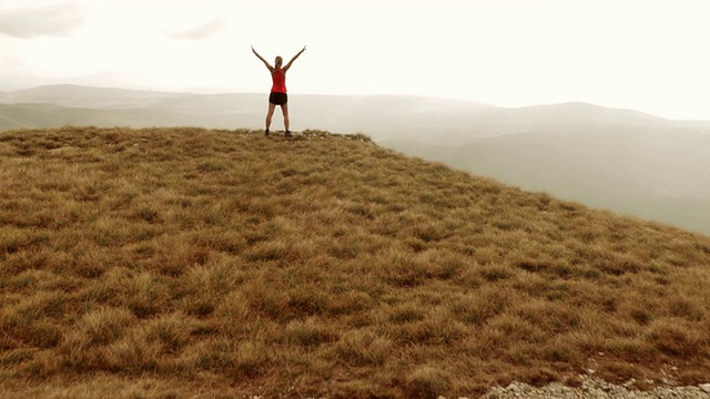 高空拍摄的女运动员在山顶举起双手视频素材