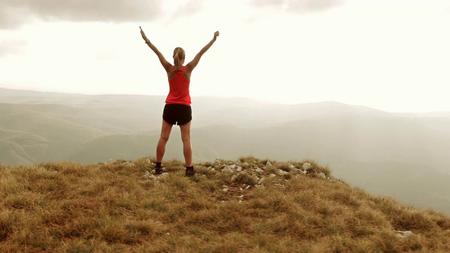 女运动员高举双手站在山脊上的航拍视频素材