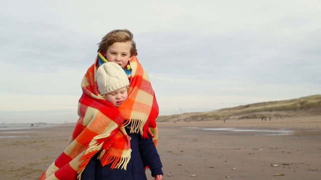 沙滩上，小男孩和小女孩裹在毯子里视频下载