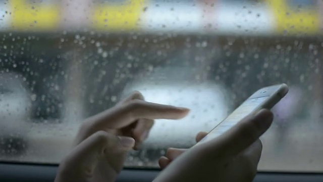 女性在雨天在车窗后使用智能手机。视频素材