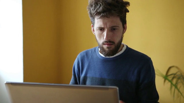 年轻帅气的蓄着胡须的男人在办公室用笔记本电脑工作视频下载