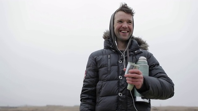 在美国蒙大拿州的乡下，一个年轻人在冬天结冰的池塘上大笑、倒热饮料、喝热饮料。视频素材