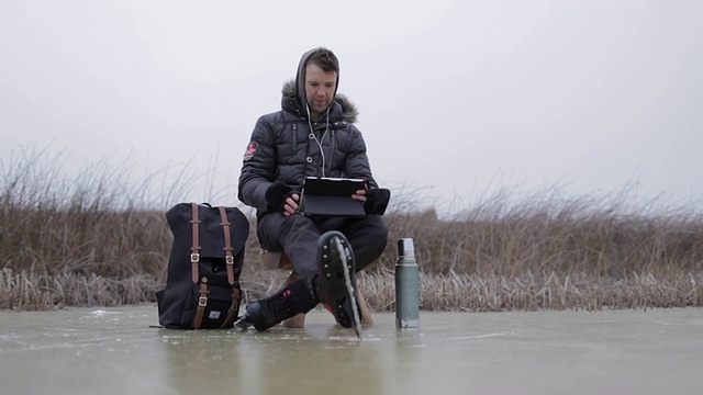 美国蒙大拿州，一个年轻人穿着溜冰鞋，在一个结冰的池塘上看着移动设备。视频下载