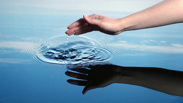 一位妇女用手指在蓝天倒映的水中画出涟漪。视频素材