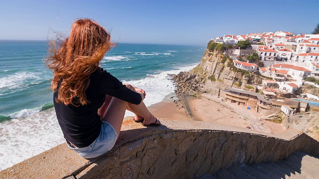 女游客俯瞰海边悬崖上的村庄视频下载