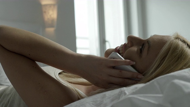 美丽的女性在床上使用电话视频下载