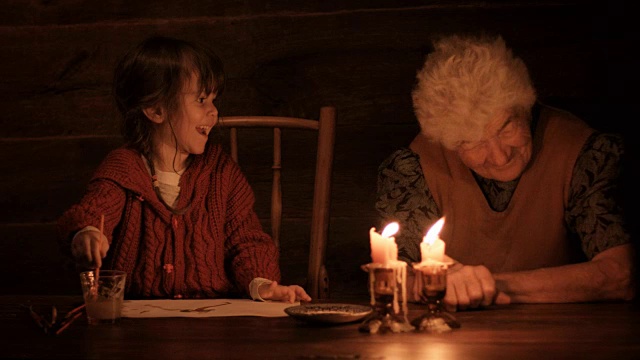 一个年轻的女孩和她的祖母在烛光下画画视频素材