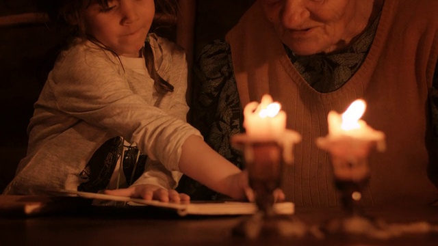 一个小女孩和奶奶在烛光下看书视频素材