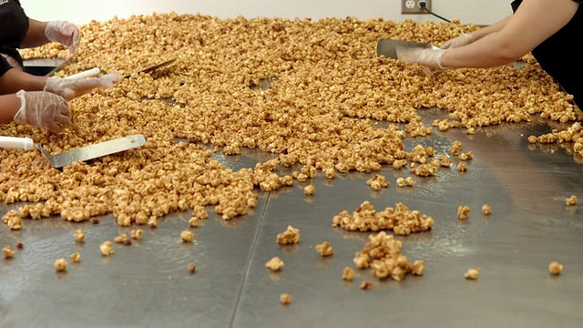 美国加利福尼亚州，女工人将杏仁太妃爆米花放在大不锈钢桌上混合并摊开视频下载