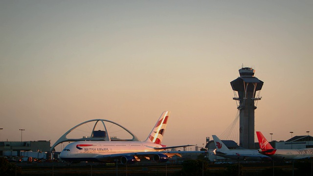 日落时分，英国航空公司(British Airways)的A-380出租车在洛杉矶国际机场(LAX)上空飞行，背景是控制塔和主题餐厅，美国联合航空公司(United Express Embraer-120)在画面中穿梭视频素材
