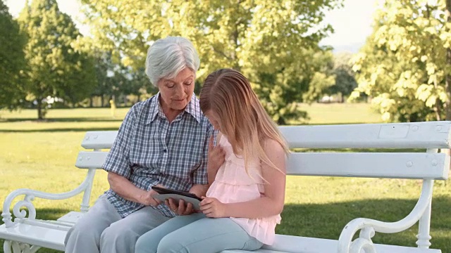 老奶奶和孙女在公园长凳上用平板电脑视频素材