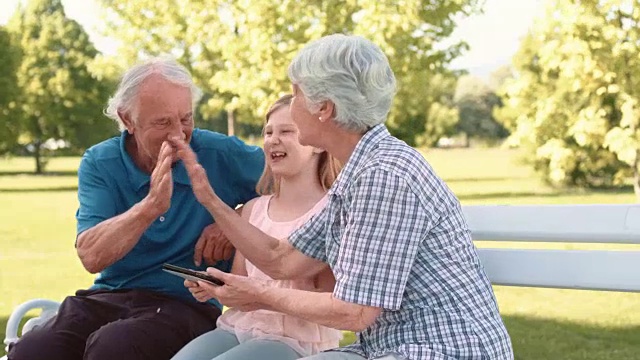 爷爷奶奶和孙女坐在公园里玩平板电脑视频素材