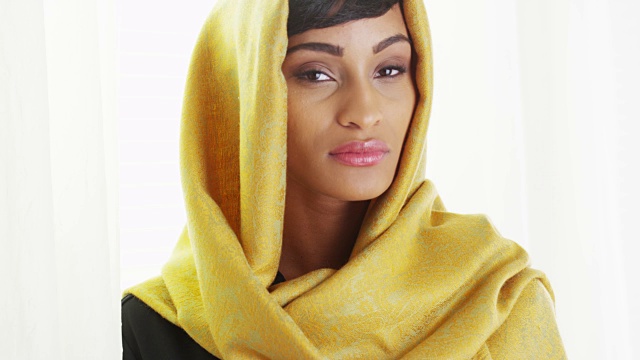 美丽的非洲妇女戴着金色头巾在明亮的房间里视频下载