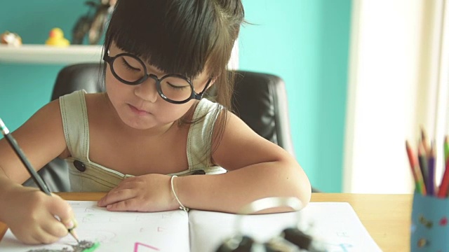 快乐的小女孩在桌子上看书和写书。视频素材