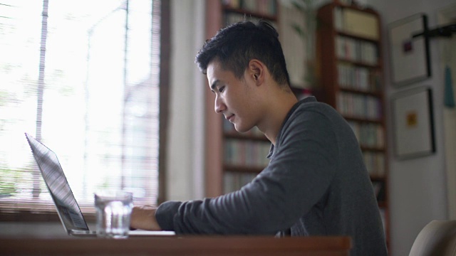 MS年轻的亚洲人在家里用笔记本电脑工作。视频素材