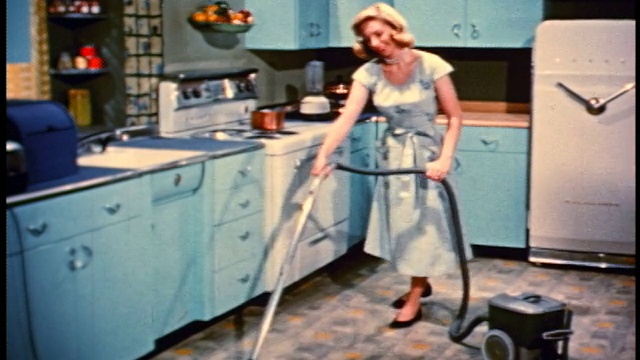 1950年，金发女人用绿色吸尘器吸尘厨房地板视频下载