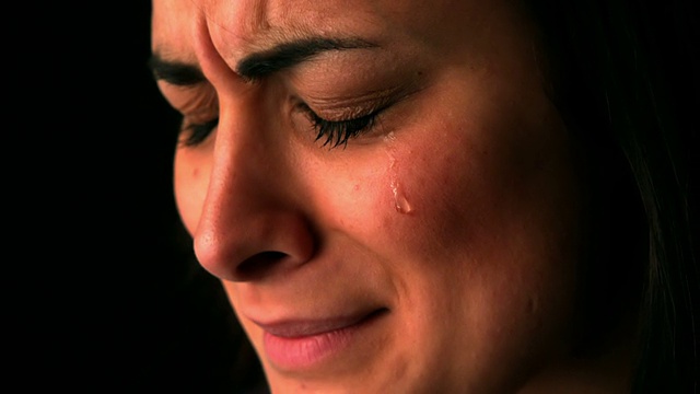 心烦意乱的黑发女人在黑色的背景哭泣视频素材