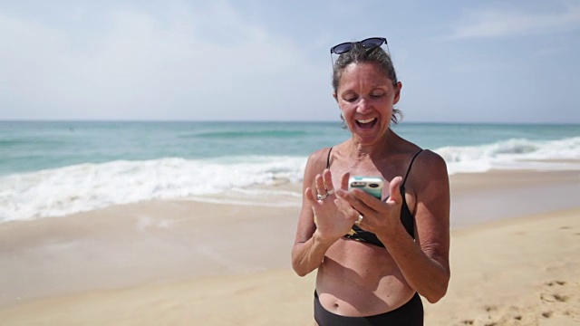 在法国南部的海滩上，一个成熟的女人正在看手机里的照片。视频下载