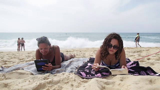 母亲和女儿在法国南部的海滩上阅读电子书和平板电脑。视频素材
