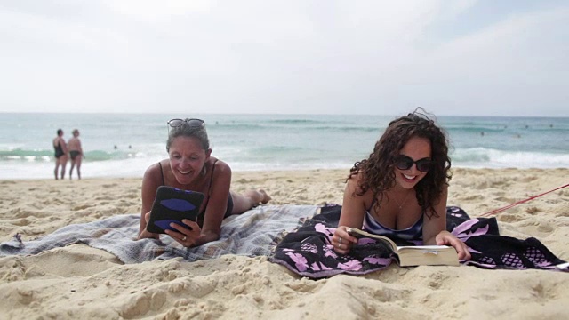 母亲和女儿在法国南部的海滩上阅读电子书和平板电脑。视频素材