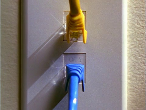 特写镜头在黄色电缆下面将蓝色电脑电缆插到墙上插座的人手上视频下载