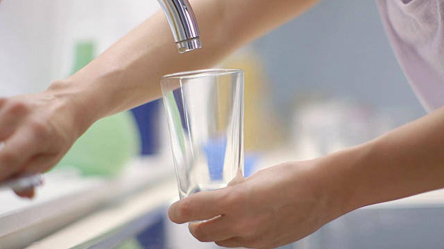 年轻女子在厨房里用水龙头往杯子里注水。视频素材