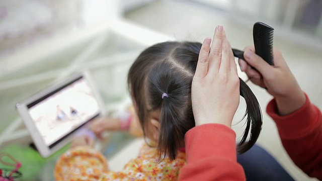 母亲给女儿梳头，女儿用手机看电影的镜头/陕西西安视频素材
