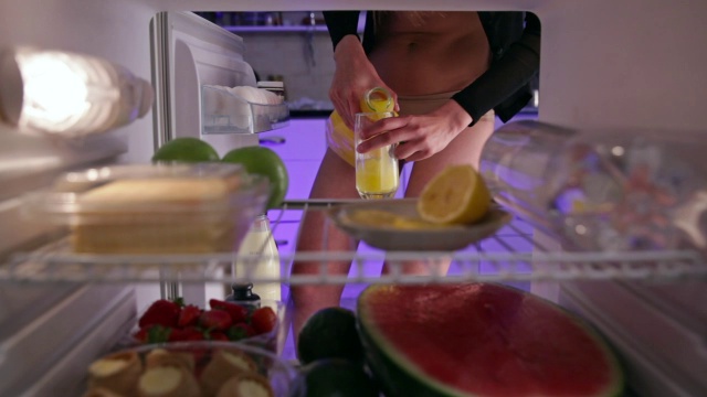穿着内衣的年轻女子从冰箱里拿出橙汁视频下载