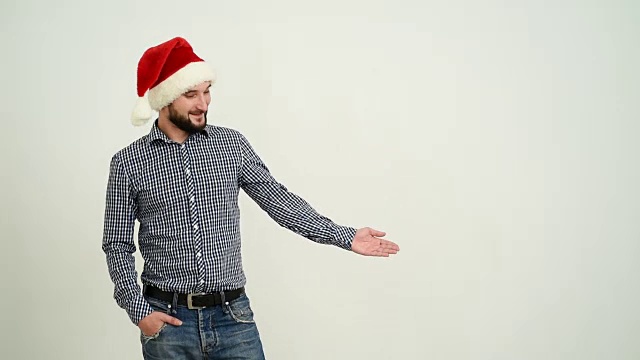 年轻的成年男子在灰色的背景上展示一顶帽子里的圣诞老人的拷贝空间视频下载