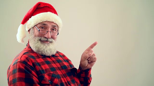 成年老人展示了一个拷贝空间，并在灰色背景上展示了圣诞老人帽子上的拇指视频下载