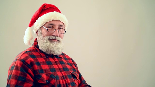 成年老人展示了一个拷贝空间，并在灰色背景上展示了圣诞老人帽子上的拇指视频下载
