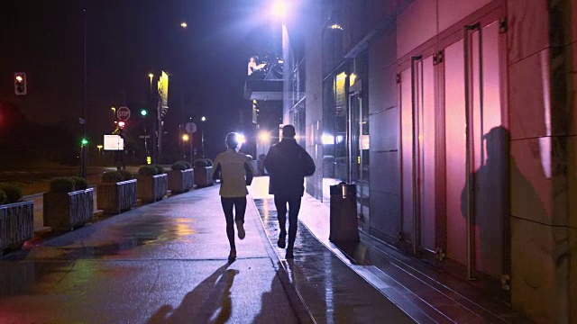 一对情侣在一个雨夜的城市街道上慢跑视频下载
