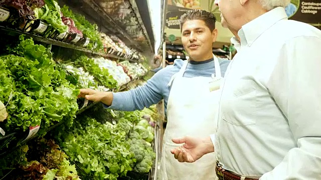 中年西班牙裔超市员工向年长的白人男性解释不同类型的莴苣视频素材