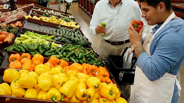 中年西班牙裔男性超市员工协助高级白人男性顾客在当地超市挑选辣椒视频素材