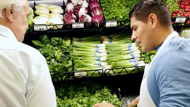 西班牙裔中年男性杂货店员工在杂货店的农产品区协助高级白人男性顾客视频素材