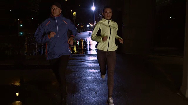 一对夫妇在雨夜的街道上慢跑视频素材