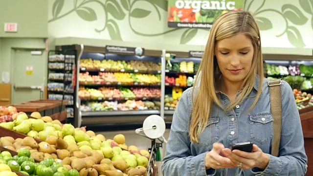 中年白人女性顾客在当地超市的农产品部检查她的智能手机购物清单视频素材