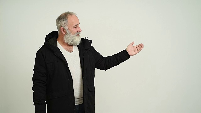 有胡须和白发的成年老人在灰色背景上显示一个拷贝空间视频下载