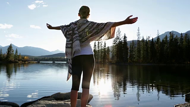 日出时，女人在湖边伸开双臂视频素材
