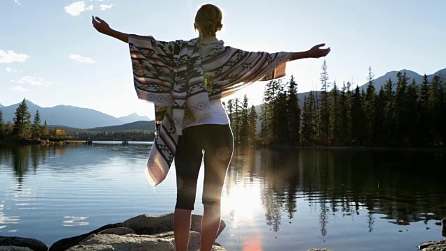 日出时，女人在湖边伸开双臂视频素材