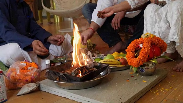 在印度教家庭中，一对夫妇和一名祭司围绕着点燃的火堆进行神庙或家庭礼拜，并提供宗教供品视频素材