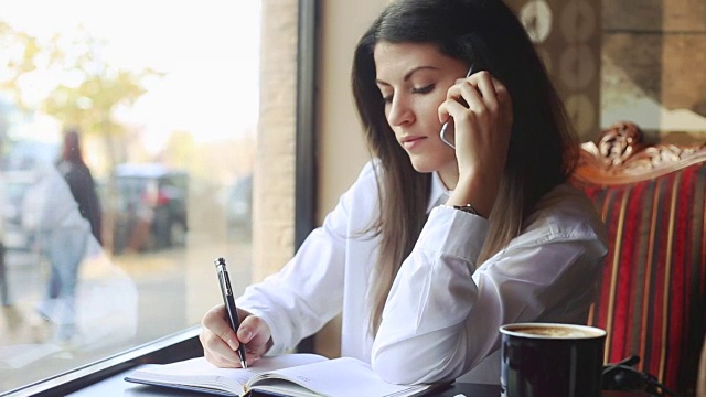 年轻的女商人一边讲电话一边写便条。视频素材