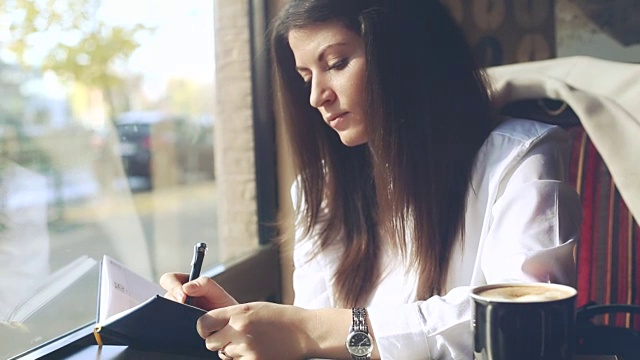 年轻的女商人边喝咖啡边写笔记。视频素材
