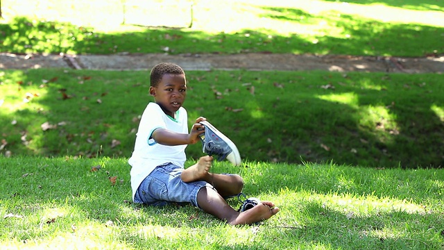 小男孩坐在草地上脱鞋视频素材