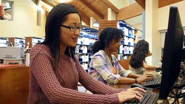 年轻的亚洲女大学生在图书馆的台式电脑上完成作业视频素材