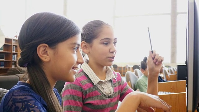 两名西班牙裔少女中学女学生正在STEM学校的图书馆里进行头脑风暴视频素材