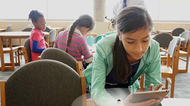 十几岁的西班牙裔女学生在STEM学校图书馆用数字平板电脑控制机器人直升机视频素材