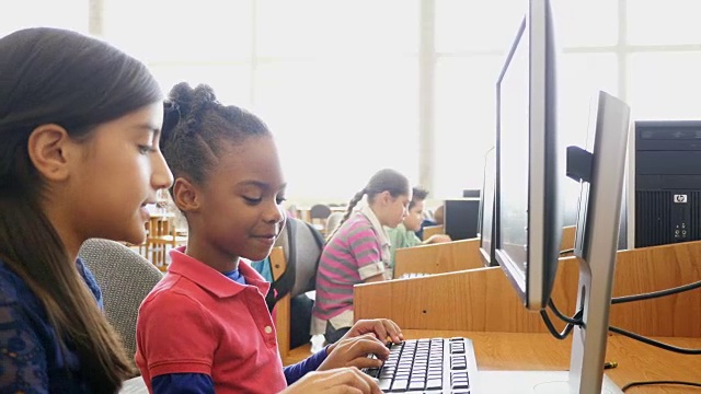 在STEM学校，一名西班牙裔女中学生在电脑上辅导一名非裔美国女小学生视频下载