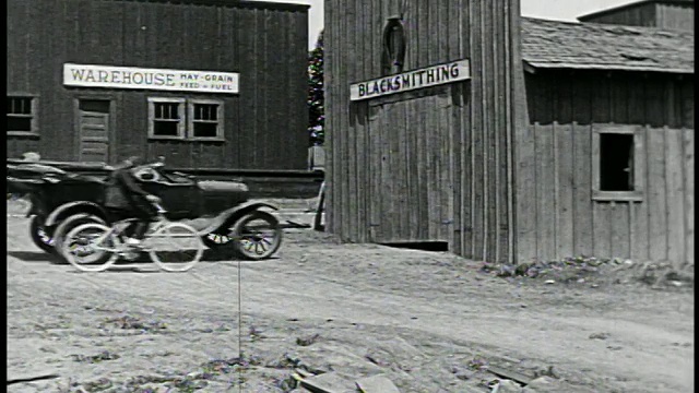 一辆1910年代/20年代的汽车撞进了铁匠店，一名男子骑着自行车经过建筑/特色视频下载