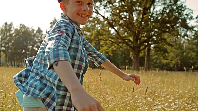 一个小男孩在阳光下跑过草地的肖像视频下载